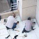 Image of two roofers laying down new material on the roof of a building at UC Davis. 