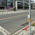 A new Accessible Pedestrian Signal (APS) device with a push button and touch-free wave sensor is mounted on a pole at a crosswalk in front of the UC Davis Mondavi Center.